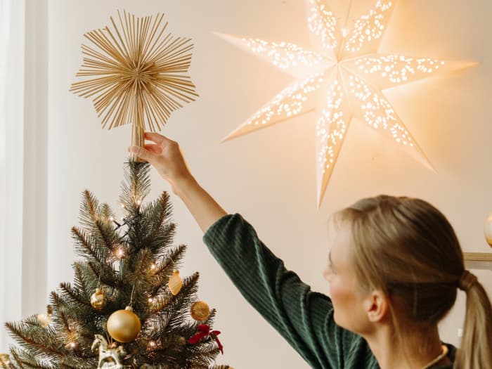 Une femme place une étoile décorative en paille au sommet du sapin artificiel FairyTrees FT01.