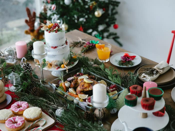 Sur la table se trouvent du poulet rôti, un gâteau de Noël et des décorations festives, avec un sapin de Noël artificiel décoré en arrière-plan.