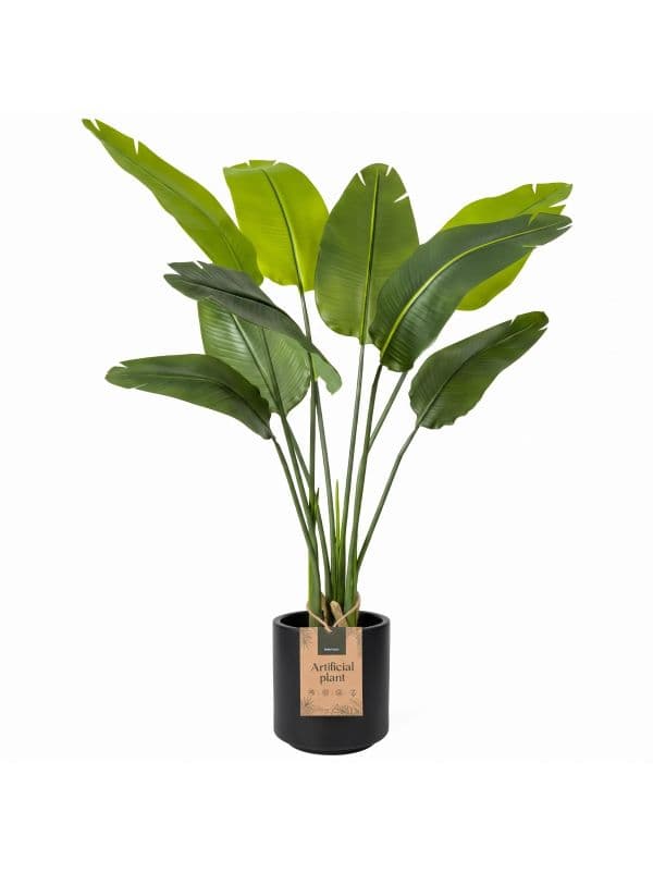 Strelitzia artificielle FairyTrees de 130 cm, aux larges feuilles allong&eacute;es sur un fond clair.