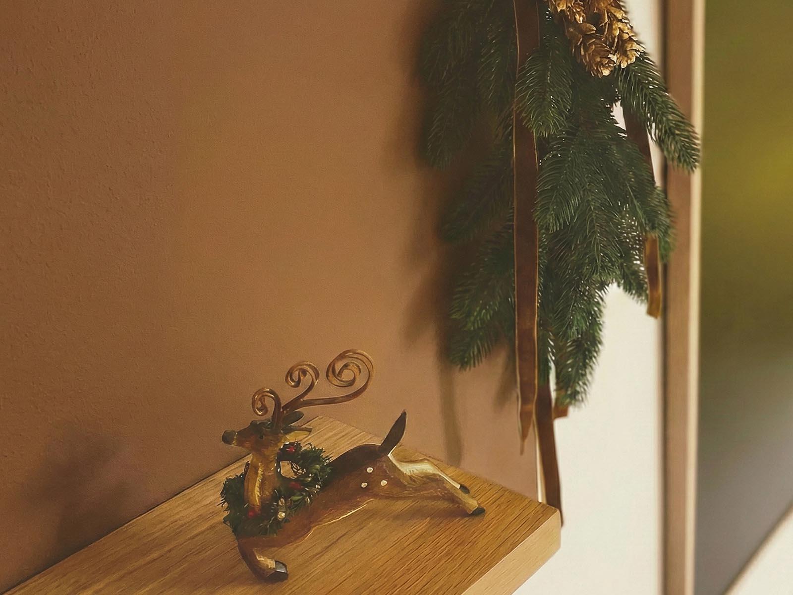 Dans le hall d'entr&eacute;e, une d&eacute;coration compos&eacute;e de branches de sapin artificiel FairyTrees et de pommes de pin est accroch&eacute;e au mur, tandis qu'une figurine de renne est pos&eacute;e sur le comptoir.