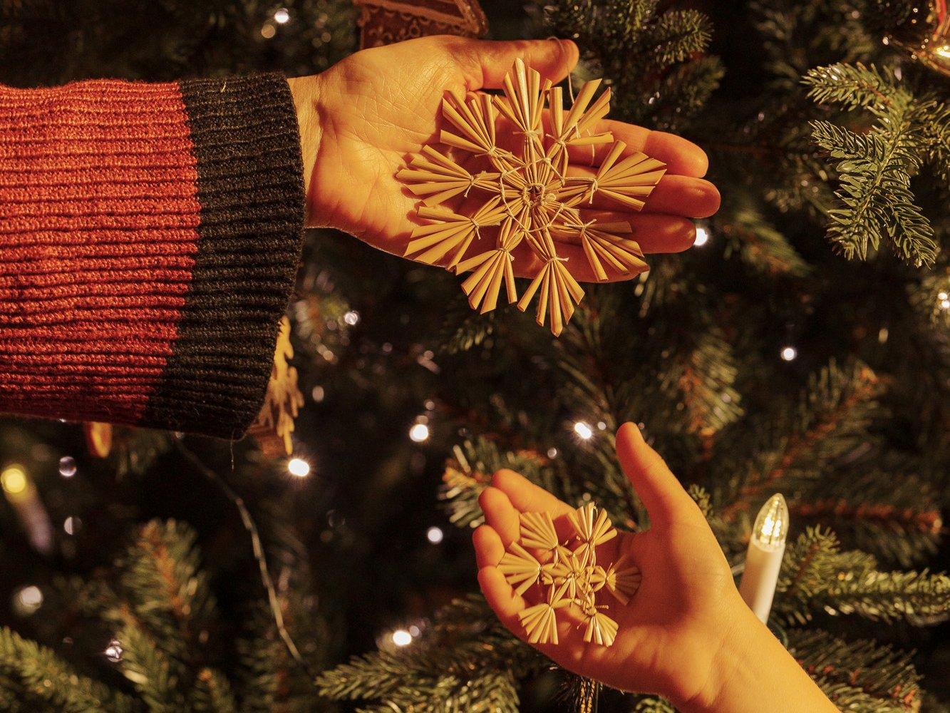Les mains de la grand-mère et de sa petite-fille tiennent des étoiles en paille près du sapin artificiel illuminé FairyTrees FT29.