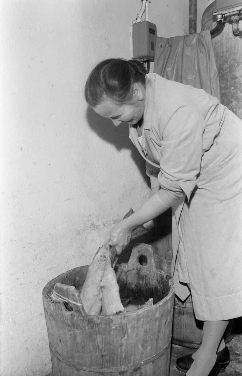Photographie du milieu du XXe si&egrave;cle montrant une femme pr&eacute;parant le lutefisk, de la morue tremp&eacute;e et rinc&eacute;e apr&egrave;s un bain de lessive alcaline, dans un cadre domestique.