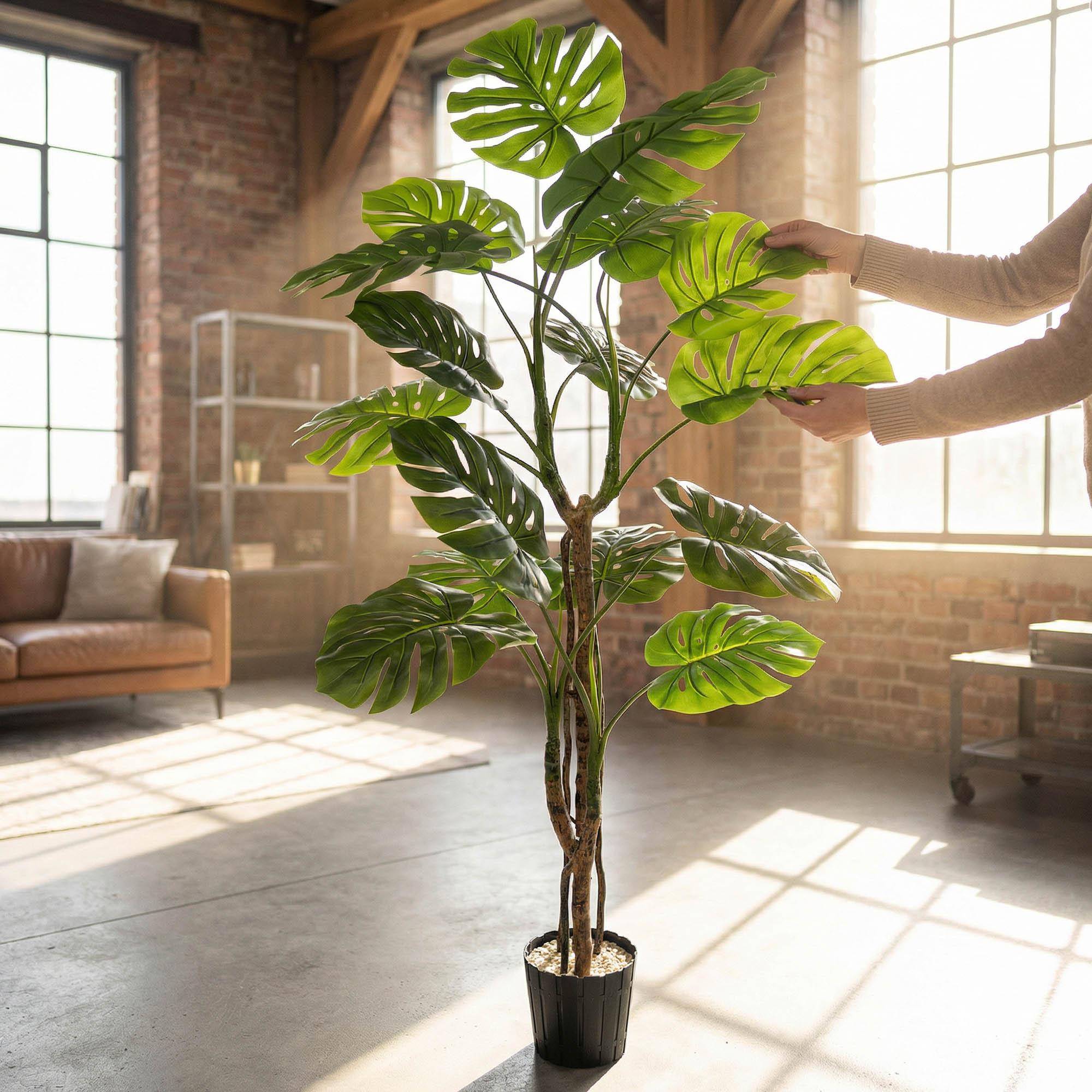Des mains ajustent les feuilles du monstera artificiel sur tige de 160 cm FairyTrees, soulignant leur aspect naturel et leur souplesse.